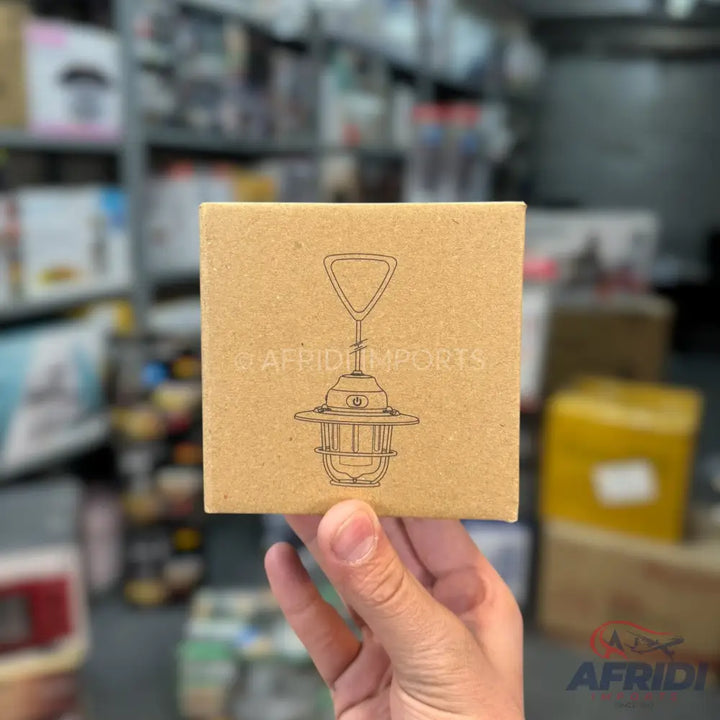 A hand holding a brown cardboard box with a line drawing of a retro-style lantern.