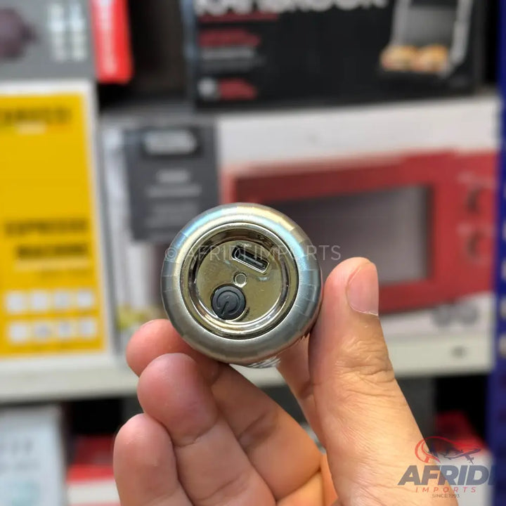 A small, cylindrical metal device with a micro-USB port and a black button on one end, held in a person’s hand.