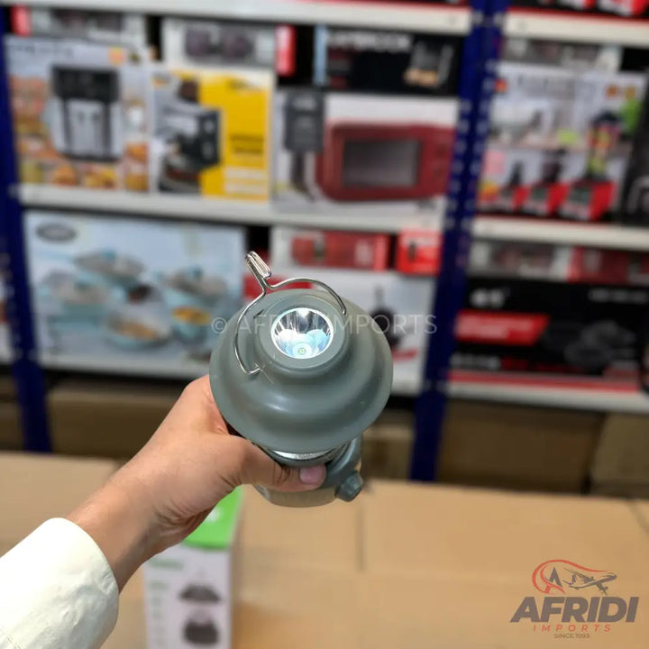 A hand holding a grey camping lantern with an illuminated LED light.