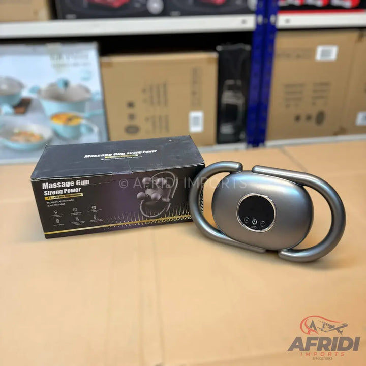 A dark grey, U-shaped massage device with a central control panel, packaged in a black box.