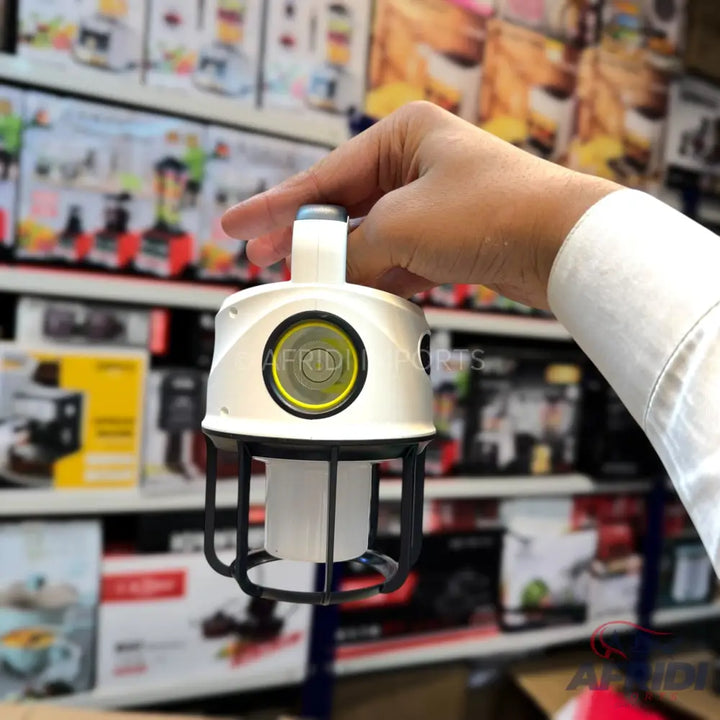 A white and black portable lantern with a bright yellow light, held by a hand.