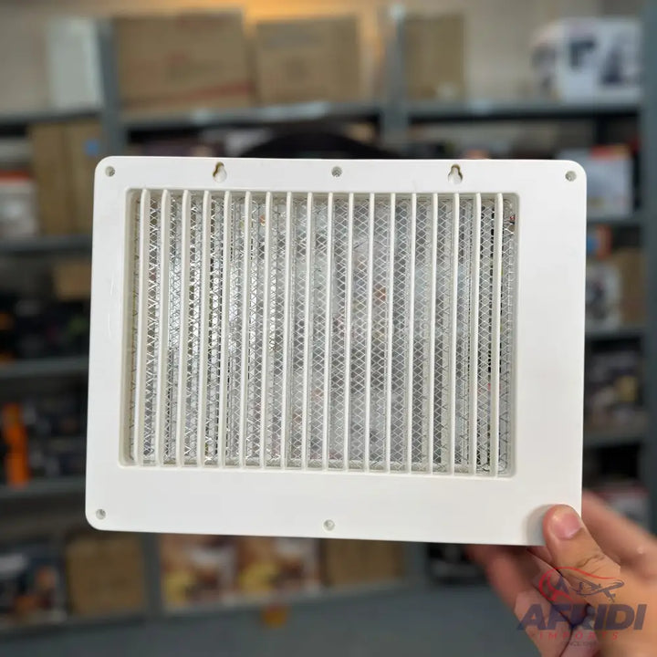 A white rectangular air vent with a mesh screen and vertical slats.