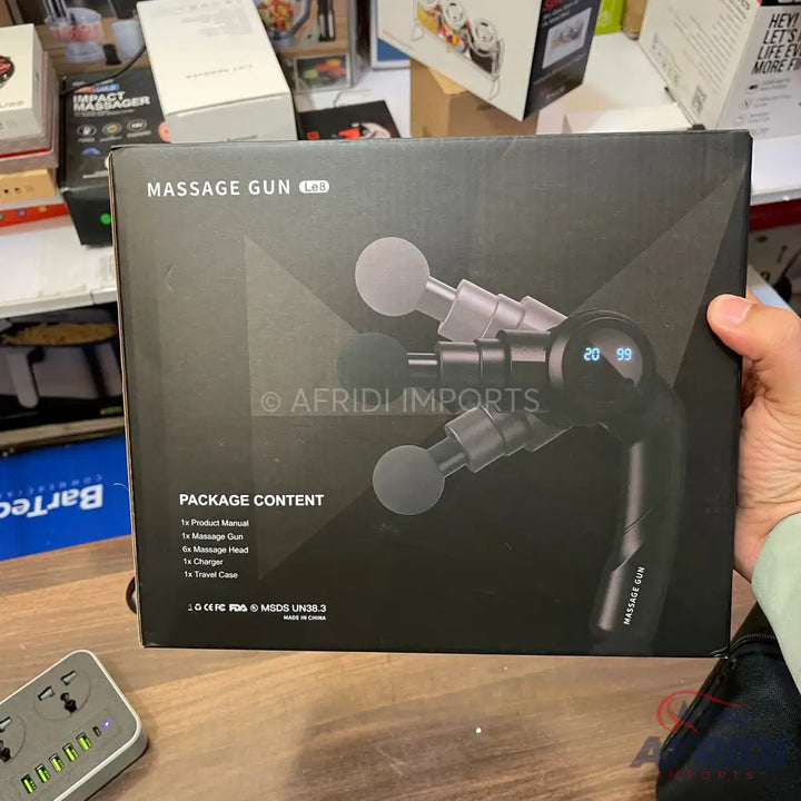 Black massage gun with multiple interchangeable heads and a digital display, packaged in a box.