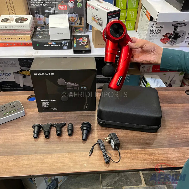 Red handheld percussive massage gun with multiple interchangeable heads and a charging cable, stored in a black carrying case.