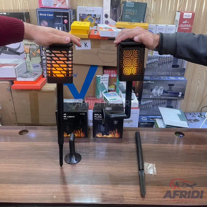 Two hands hold two solar-powered LED flickering flame garden lights.