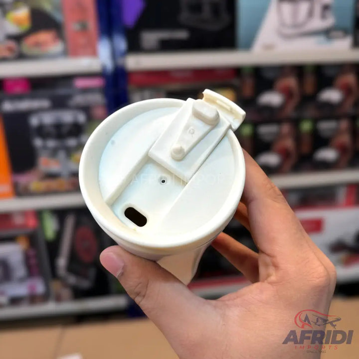 Hand holding a white travel mug with a flip-top lid.