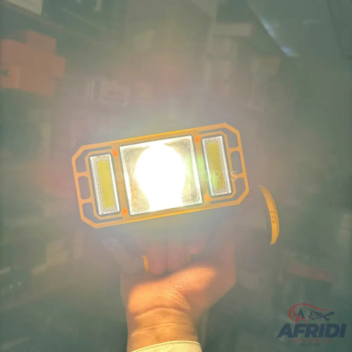 A handheld, rectangular work light with a bright central LED and two smaller side LEDs, encased in a durable yellow frame.