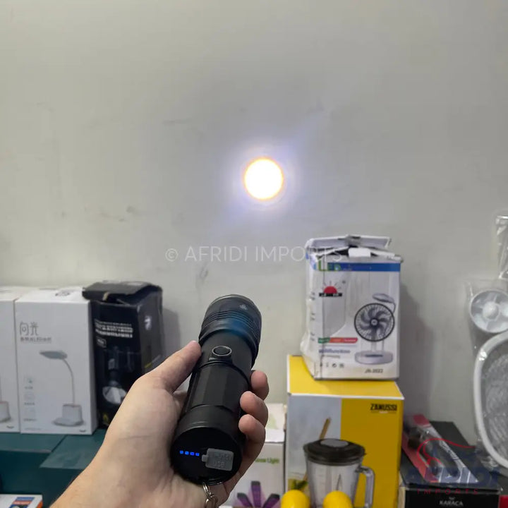 Hand holding a black flashlight with a blue indicator light and a bright beam.