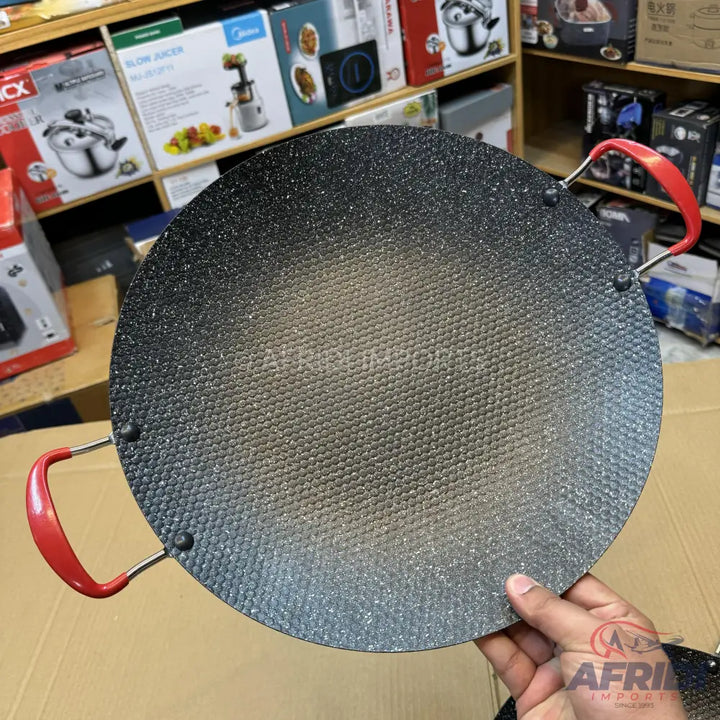 Round, black, textured non-stick griddle with two red handles.