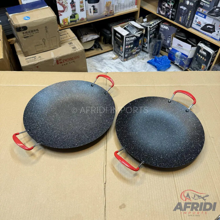 Two round, flat, black cooking griddles with red handles.
