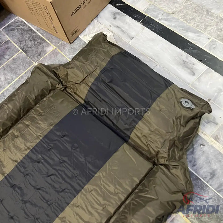 An olive green and dark gray striped self-inflating camping pad with an air valve.