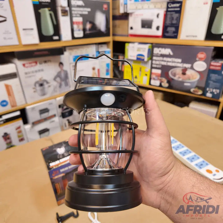 A black solar-powered camping lantern with a clear glass body and an internal LED filament.