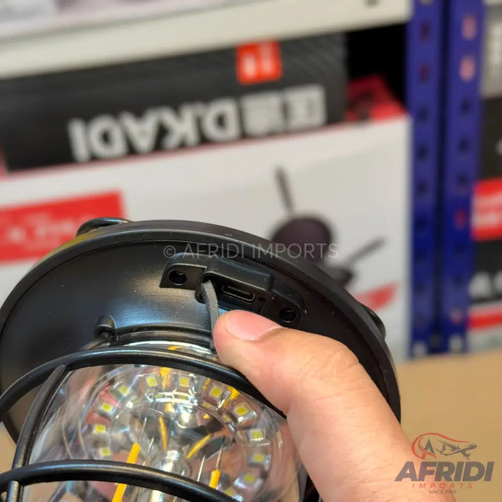 A person’s hand plugging a charging cable into a black, vintage-style camping lantern with exposed LED filaments.