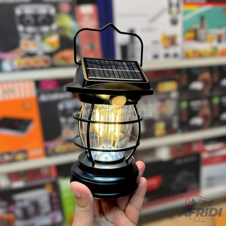 A black solar-powered lantern with a clear glass globe and a warm LED light.