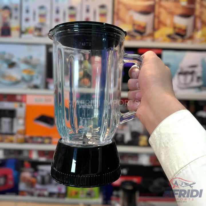 A glass blender jar with a black lid and base, held by a hand.