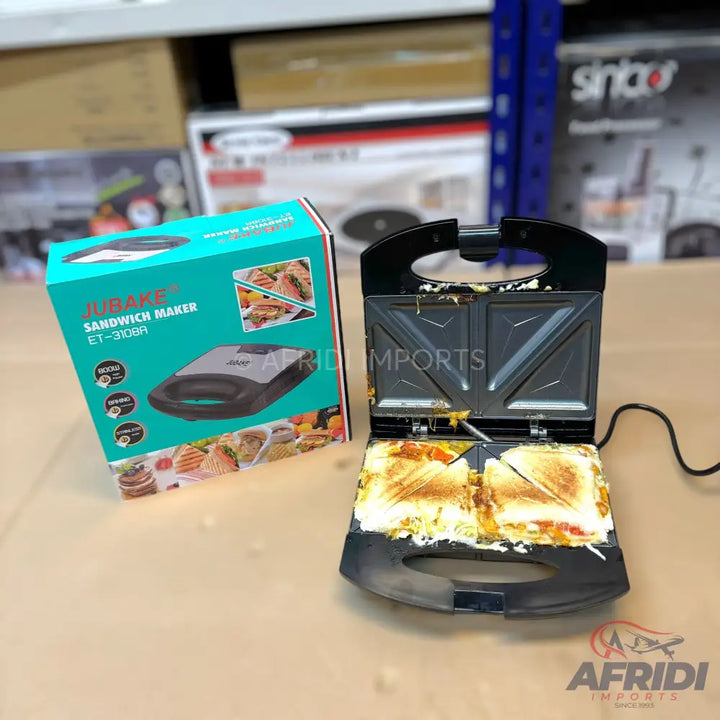 An open sandwich maker with two golden-brown, triangular sandwiches inside, alongside its teal and black product box.