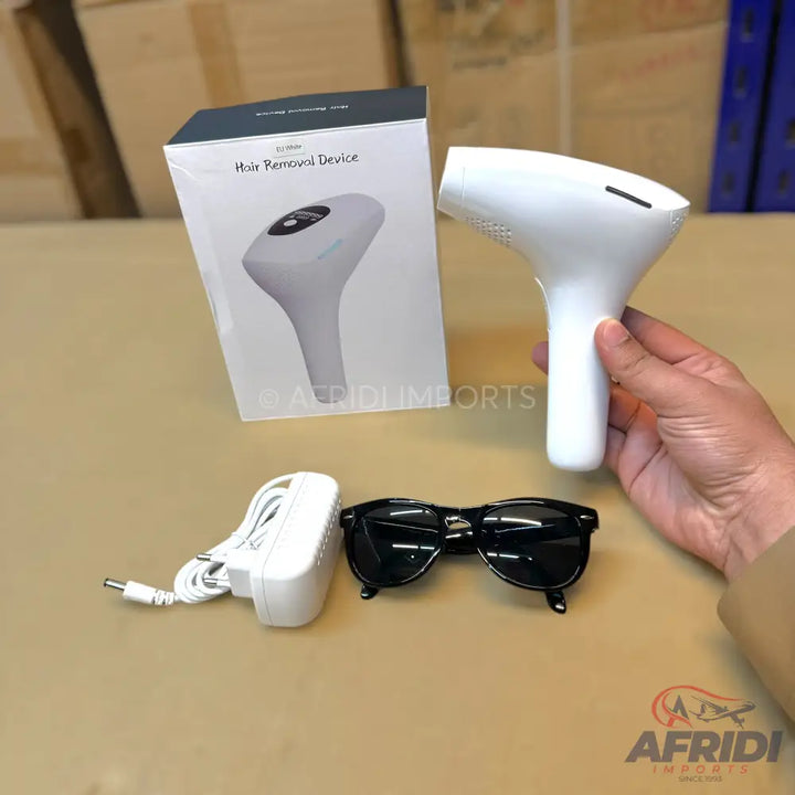 A white handheld hair removal device with its packaging, power adapter, and protective eyewear.