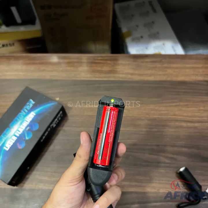 A black flashlight with two red batteries visible inside and a green indicator light.