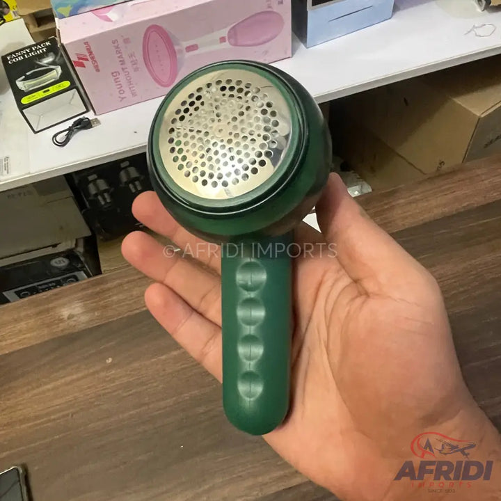 Handheld dark green lint remover with a perforated metal head.