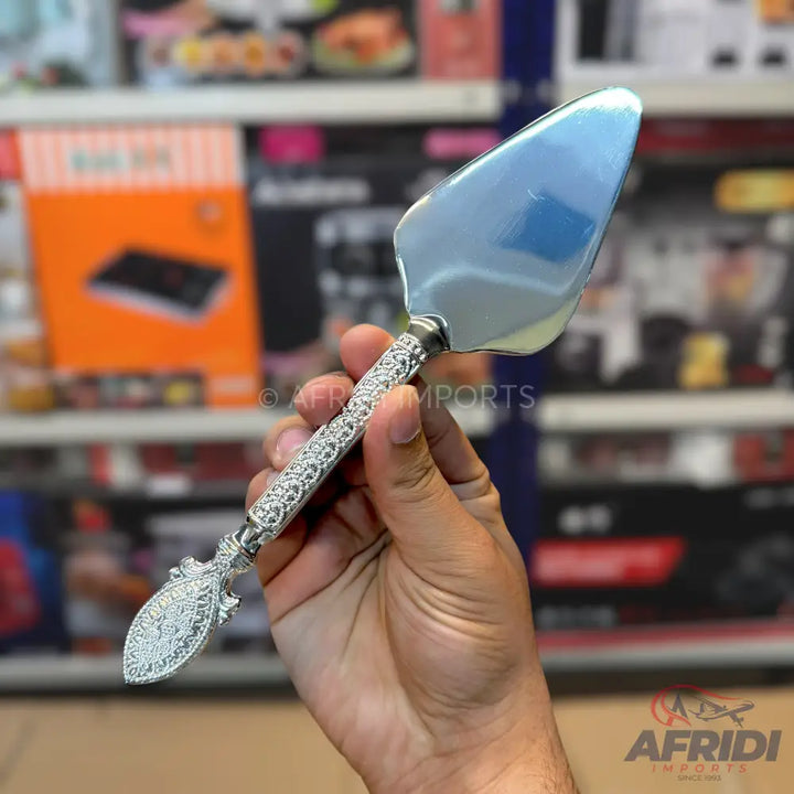 A silver cake server with an elaborately decorated handle.