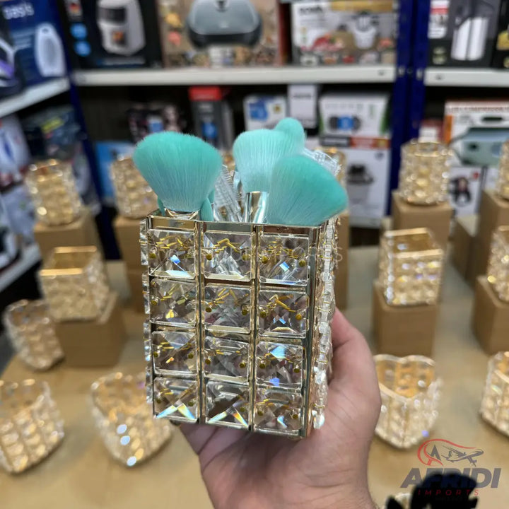 A crystal-studded makeup brush holder containing several teal-colored brushes.