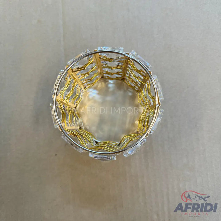 A cylindrical decorative container with a gold-colored wire mesh interior and clear crystal-like embellishments on the exterior rim.