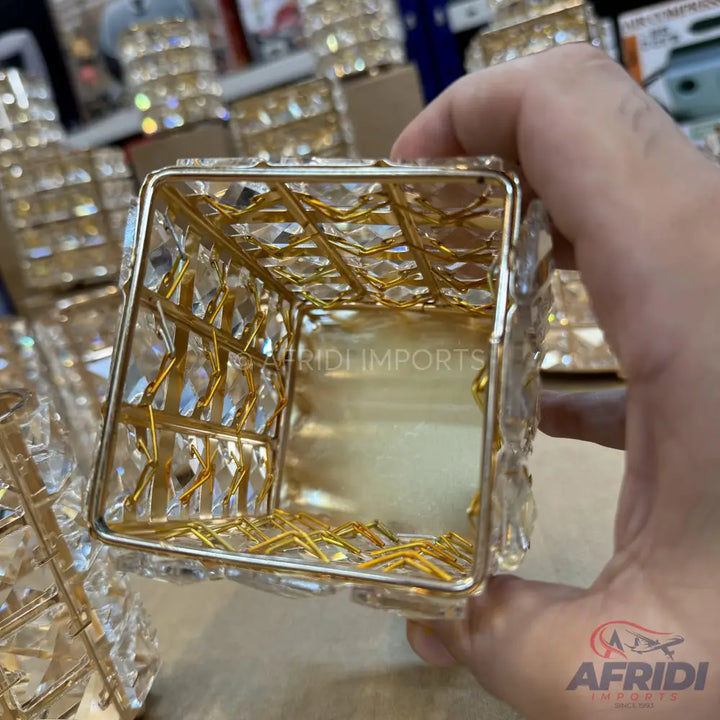 A decorative square-shaped container with a gold metal frame and clear crystal-like panels.
