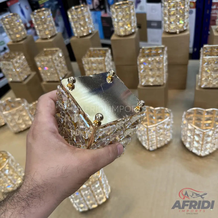 Hand-held square crystal tea light holder with a gold-colored top and decorative feet.