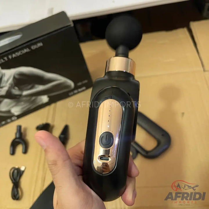 Black and gold handheld massage gun with multiple interchangeable heads and a charging cable.