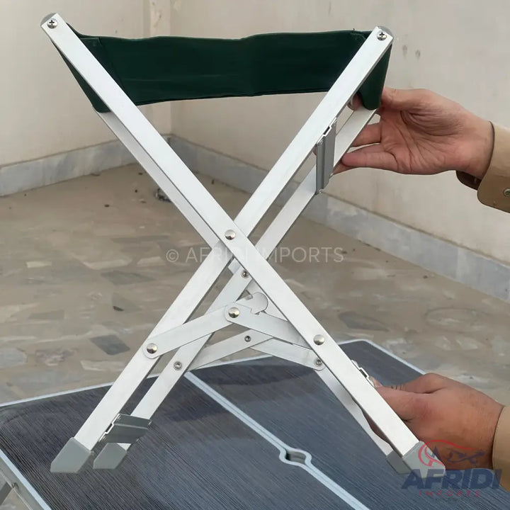 Collapsible camping stool with a dark green fabric seat and a silver aluminum frame.