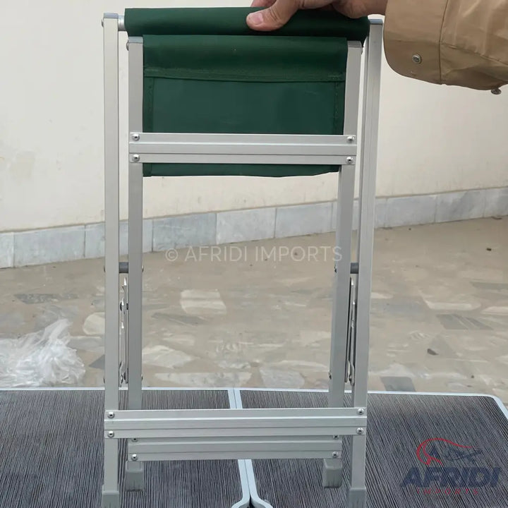 A collapsible camping stool with a green fabric seat and silver metal frame.