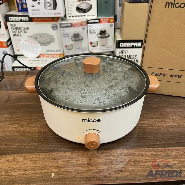 White electric cooking pot with a clear glass lid and light brown handles and control knob.