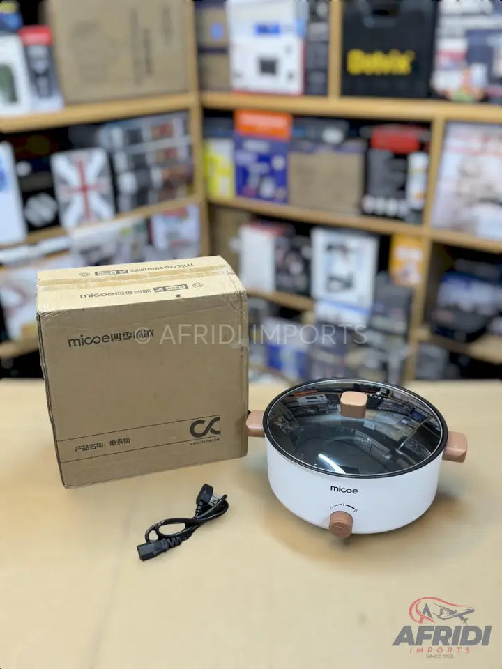White electric cooking pot with a glass lid and light brown wooden accents, accompanied by its power cord and packaging box.
