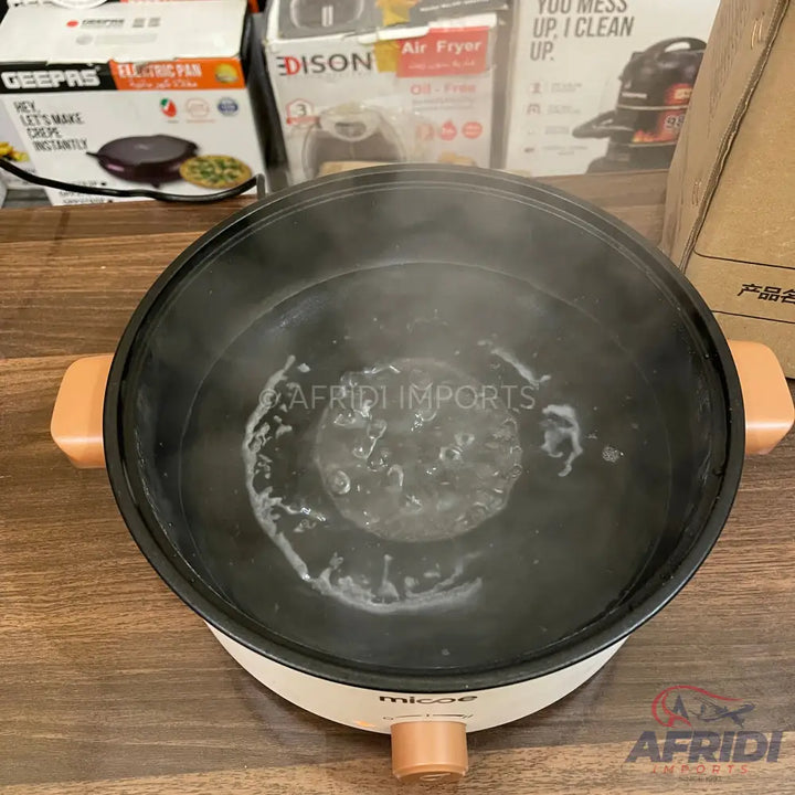 A non-stick electric cooking pot with a white base and peach-colored handles, containing boiling water.