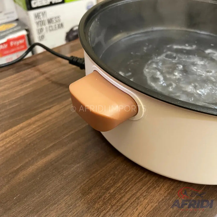 A cream-colored electric cooking pot with a brown handle, containing bubbling water.