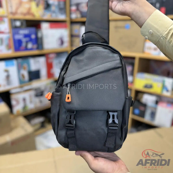 Dark gray sling bag with an orange zipper pull and two front buckles.