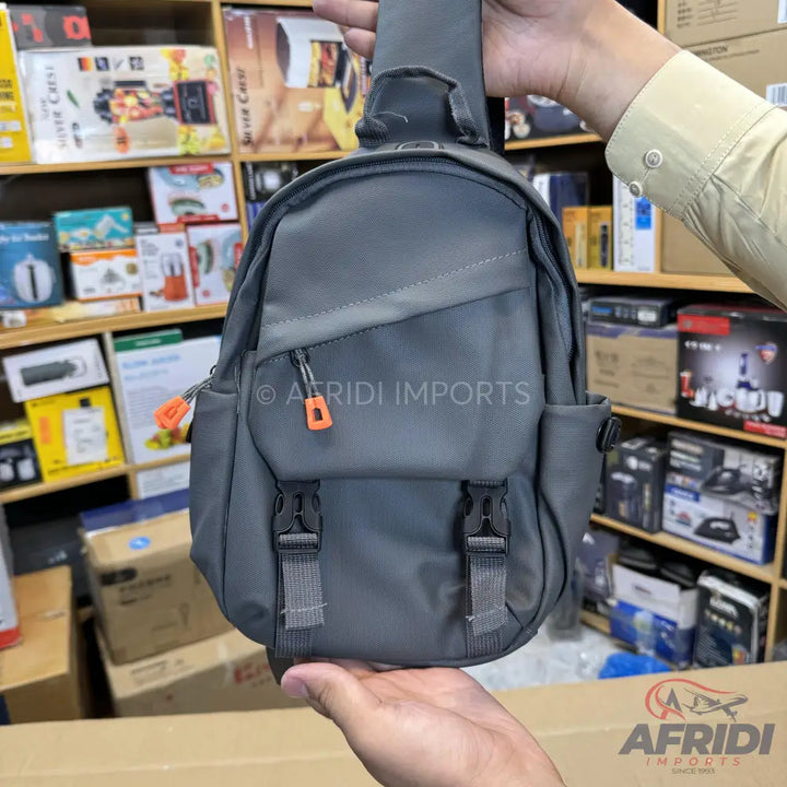 Gray single-strap sling backpack with orange zipper pulls and front buckles.