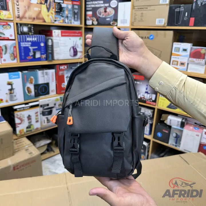 Dark grey sling backpack with orange zipper pull tabs and black buckle closures.
