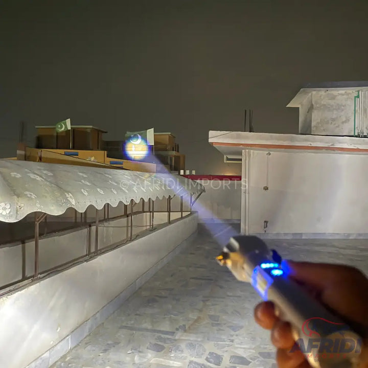 A handheld, silver-colored laser pointer emitting a blue beam, with blue indicator lights visible on its side.