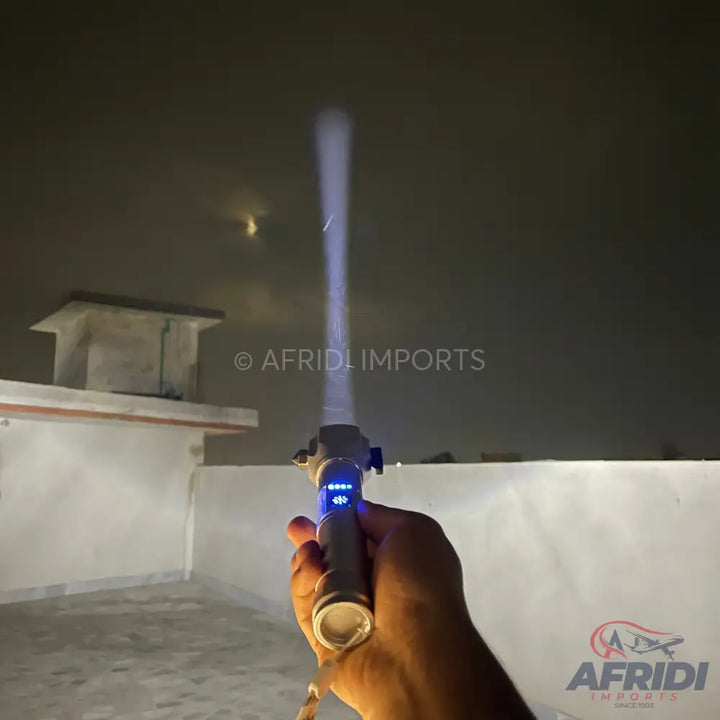 A handheld, gray flashlight with a blue digital display and a bright, focused beam of light.