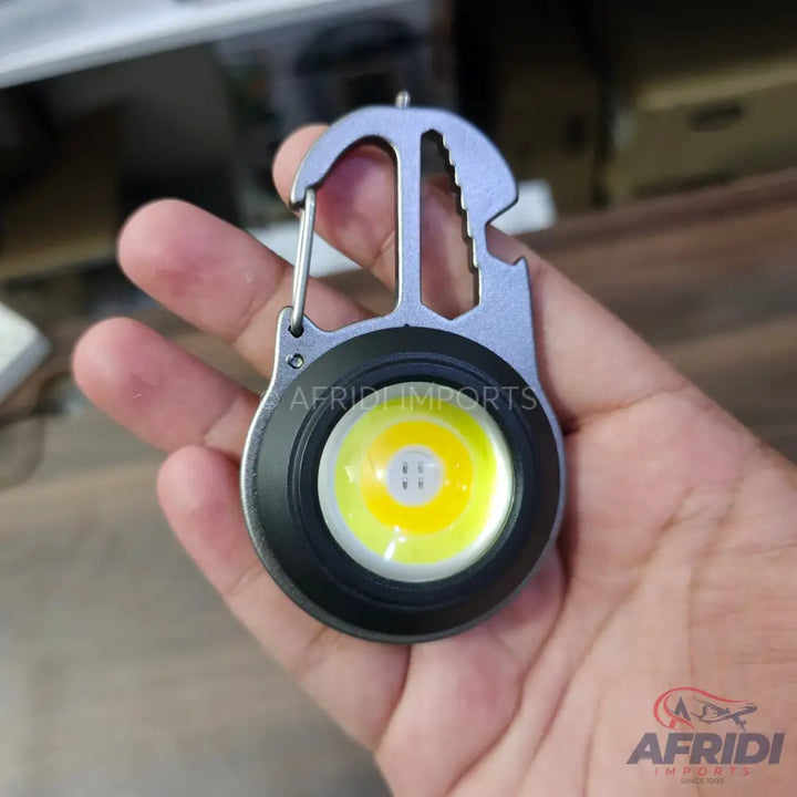A metallic multi-tool keychain with an integrated LED flashlight.