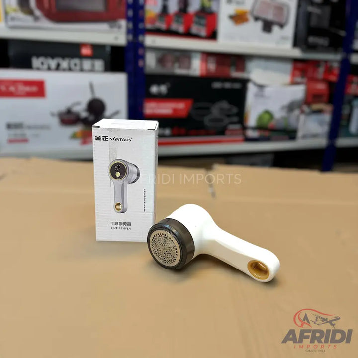 A white lint remover with a dark gray and gold-colored head, packaged in its white box.