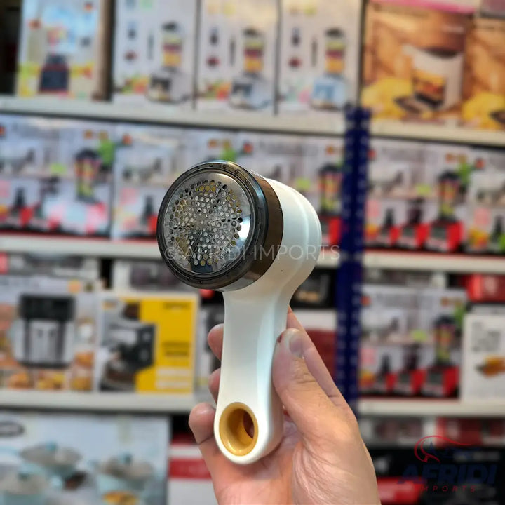 White handheld fabric shaver with a metallic, perforated head and a brown-orange accent on the handle.