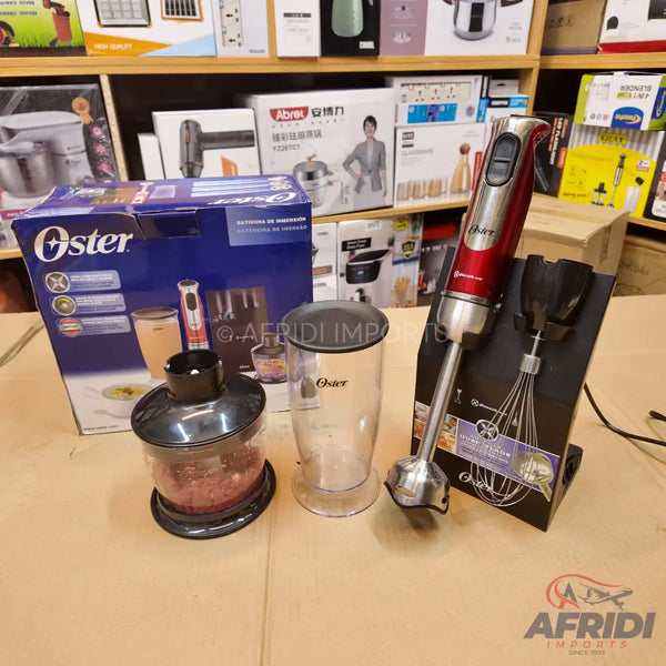A red and silver Oster immersion blender set with chopper and measuring cup attachments.