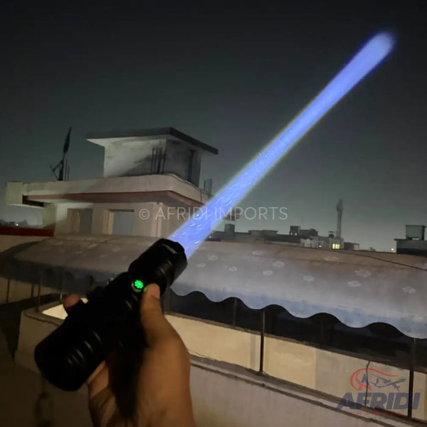 Hand holding a black flashlight emitting a long blue beam.