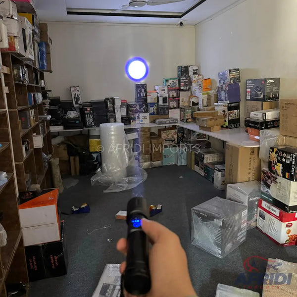A handheld black flashlight with a blue light beam projecting onto a wall.