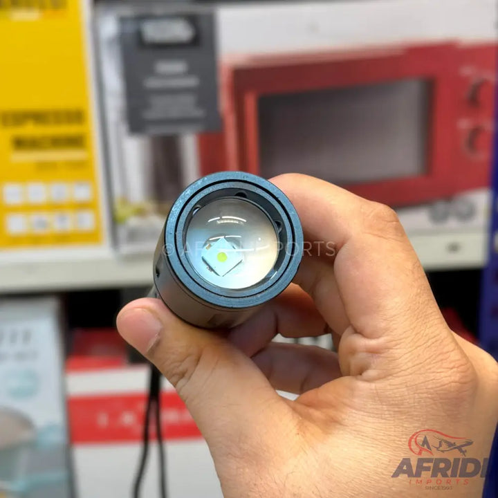 A hand holding a flashlight with a clear lens and a bright, square-shaped LED emitter.