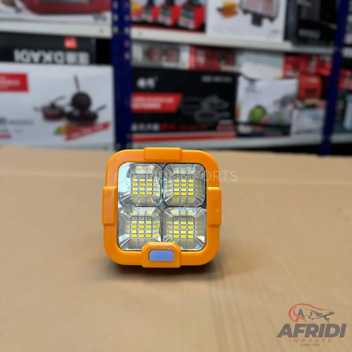 An orange-framed square LED light with four panels of bright, cool-toned bulbs.