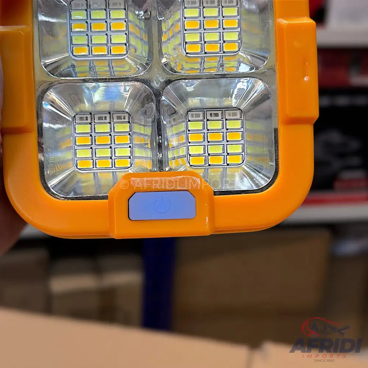 An orange-cased LED light with four bright white and yellow panels.