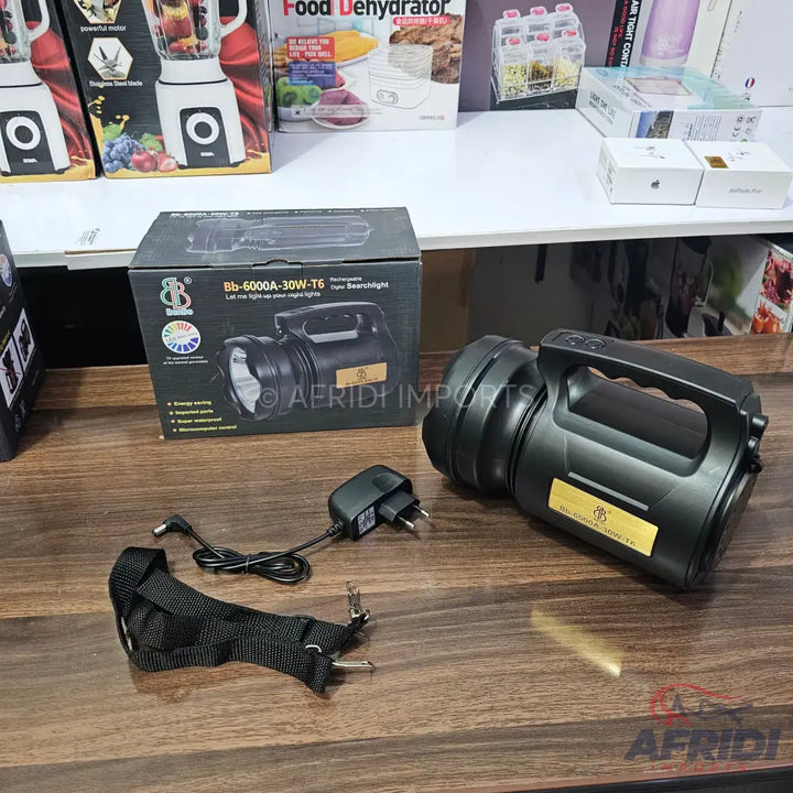 A black, handheld spotlight with a power adapter and shoulder strap.